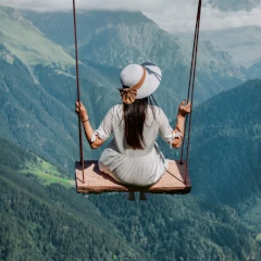 Kobieta siedząca na huśtawce zawieszonej wysoko nad górską doliną