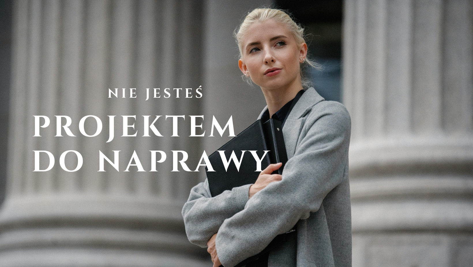 Kobieta w szarym płaszczu z teczką na tle kolumn