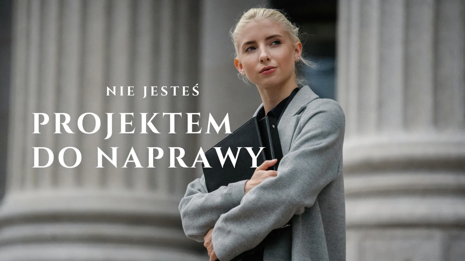 Kobieta w szarym płaszczu z teczką na tle kolumn