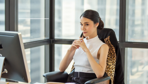 Kobieta w eleganckim stroju siedzi przy biurku w nowoczesnym biurze z widokiem na miasto